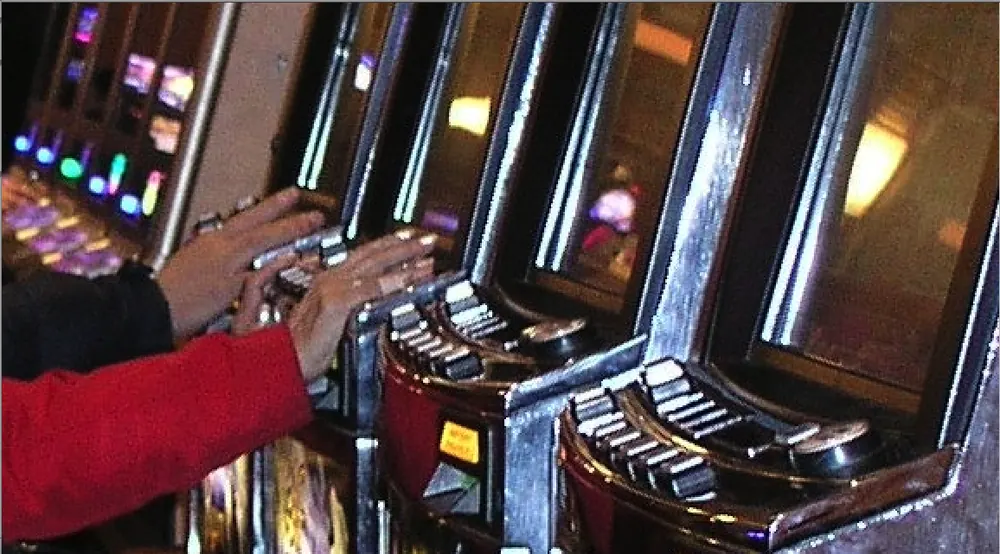 Hands on the spin buttons of a row of slot machines, illustrating how slot sessions vary - high volatility vs low volatility slots