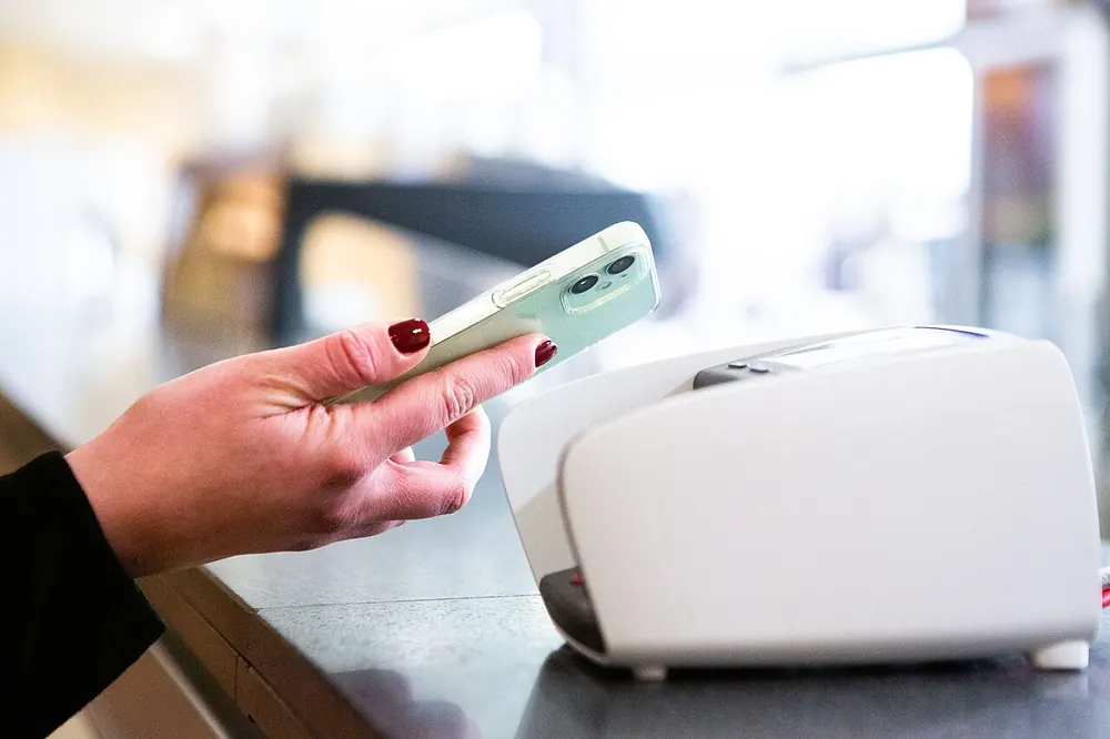 maya to usdt - Hand holding a smartphone near a payment terminal, representing e-wallet crypto purchases